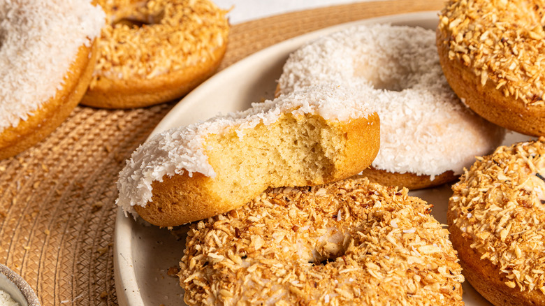 Coconut baked donut with a bite off next to other donuts