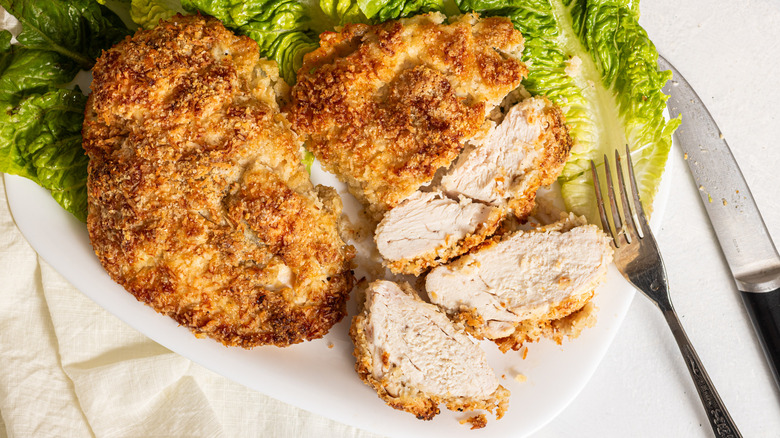 Two crispy coconut baked chicken breasts with one sliced into bite size pieces on a plate with lettuce