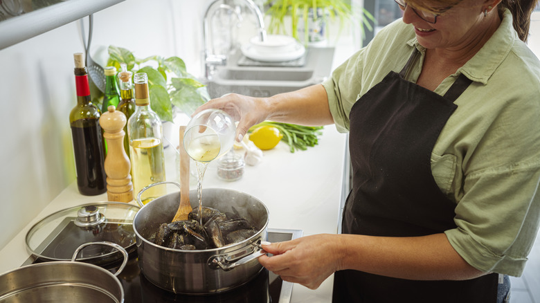 Woman pours white cooking wine into a pot of mussels