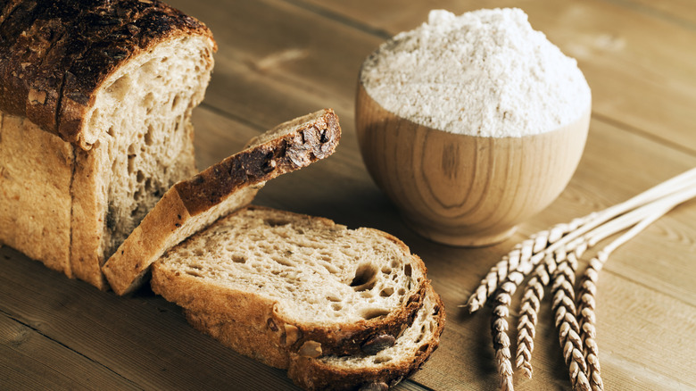 Bowl with bread flour and loaf of bread