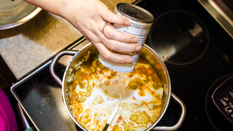 hand pouring coconut milk into soup on stove