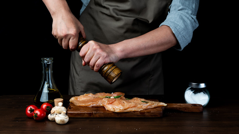 Man in apron grinds fresh black pepper on raw meat.