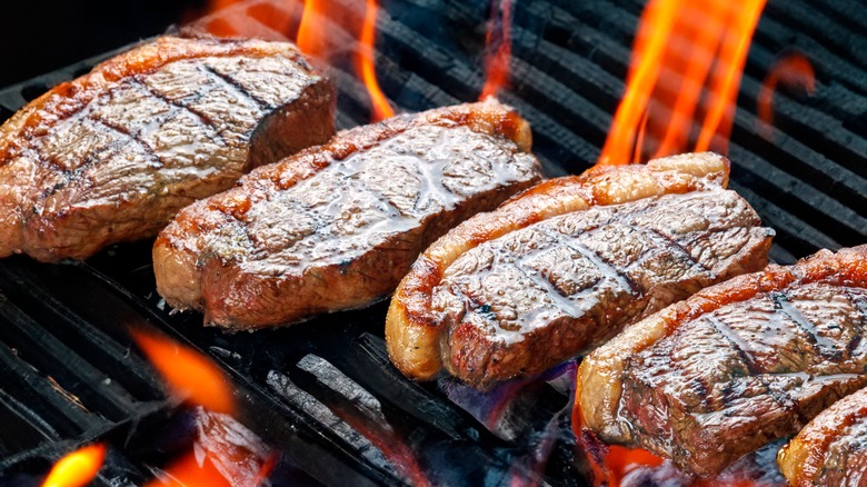 4 steaks sitting on a flame grill.