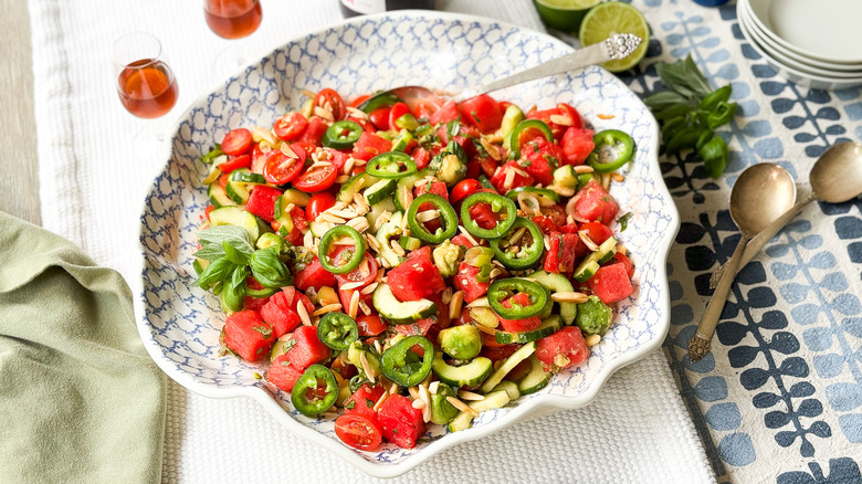 Deconstructed watermelon gazpacho salad in serving bowl with spoons and sherry glasses on table