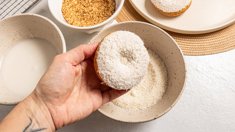 Holding a donut with glaze and shredded coconut