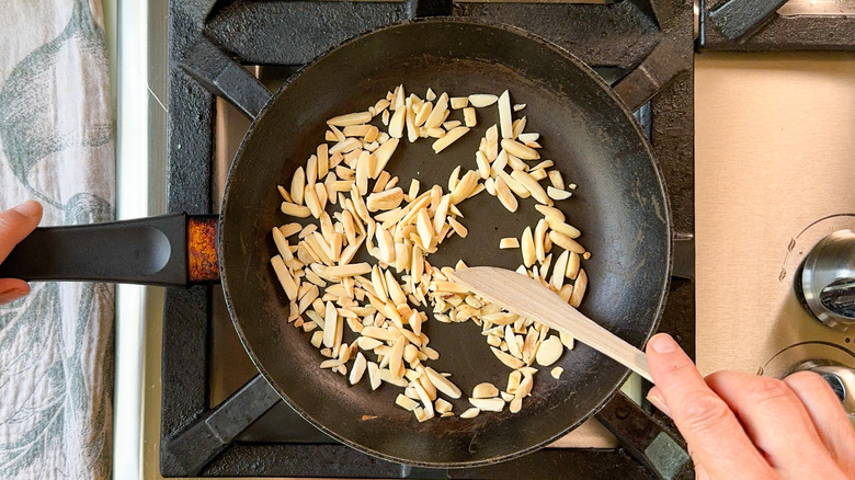 Toasting slivered almonds in skillet with wooden spoon over stovetop