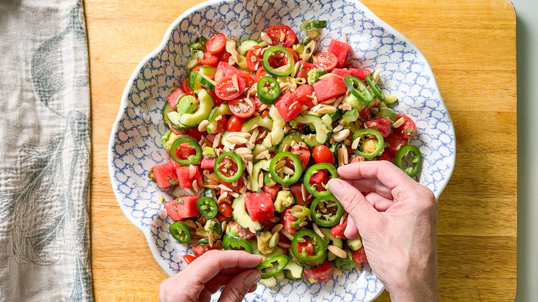 Garnishing deconstructed watermelon salad in serving bowl with jalapeño slices and toasted almonds