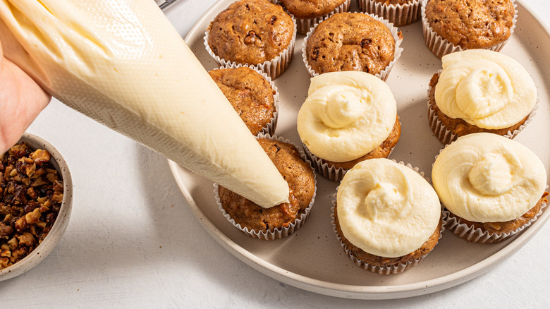 Piping cream cheese frosting over cupcakes