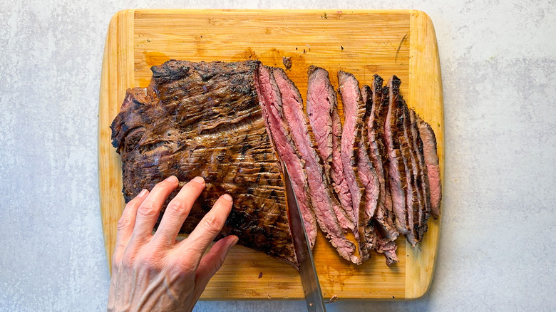 Slicing grilled flank steak against the grain on carving board