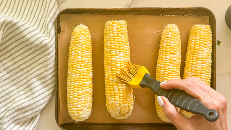 hand brushing oil on corn