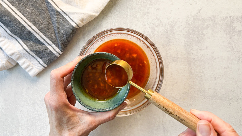 Scooping out grilled flank steak taco marinade into a small bowl with a tablespoon