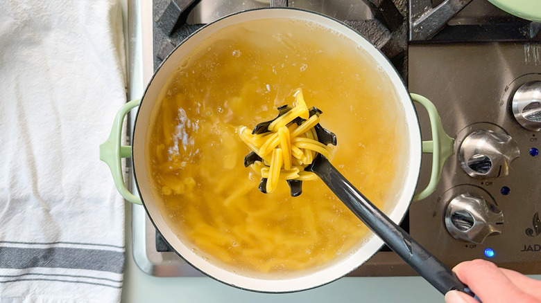 Pasta cooking in pot on stovetop with pasta spoon