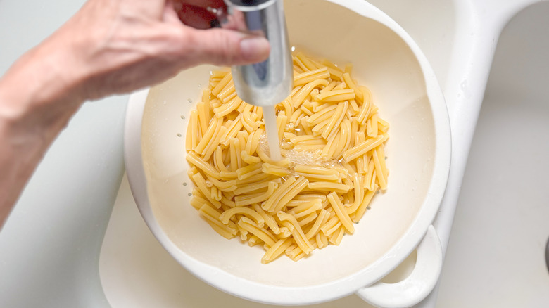 Rinsing cooked pasta in colander in sink with cold water