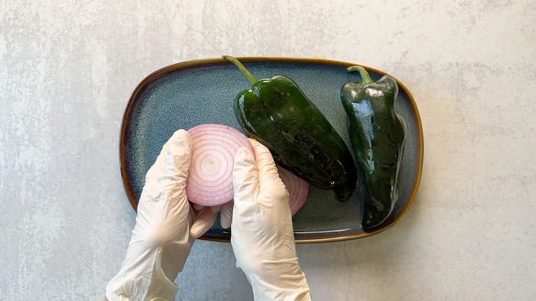 Rubbing red onion and poblano peppers with olive oil using gloves