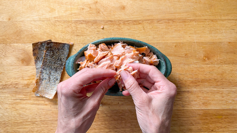 Breaking up hot smoked salmon with fingers into dish