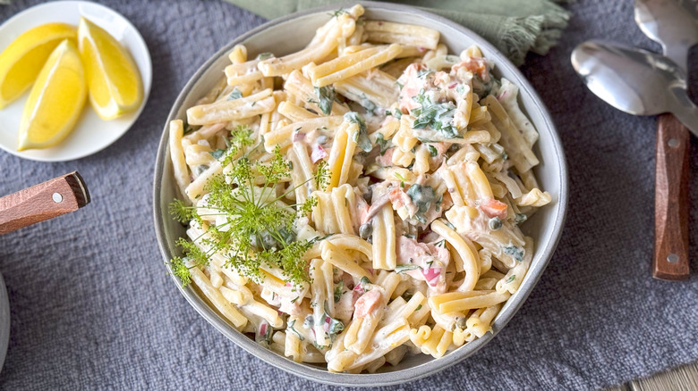 Salmon dill pasta salad in serving bowl with lemon wedges