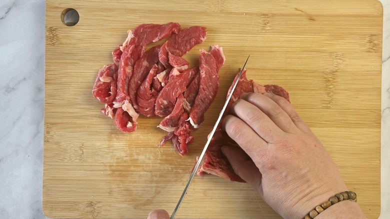 hand with knife cutting steak